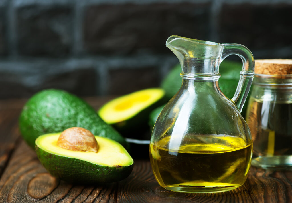 Pitcher of avocado oil on wooden table with avocados