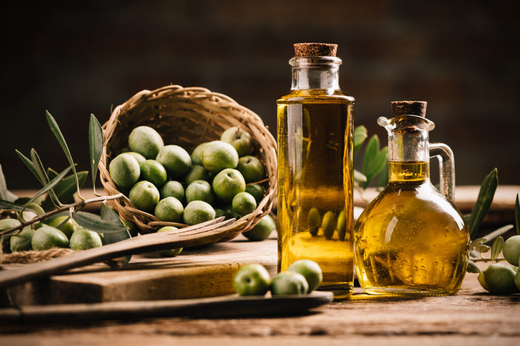 Bottle of olive oil on wooden table with basket of olives